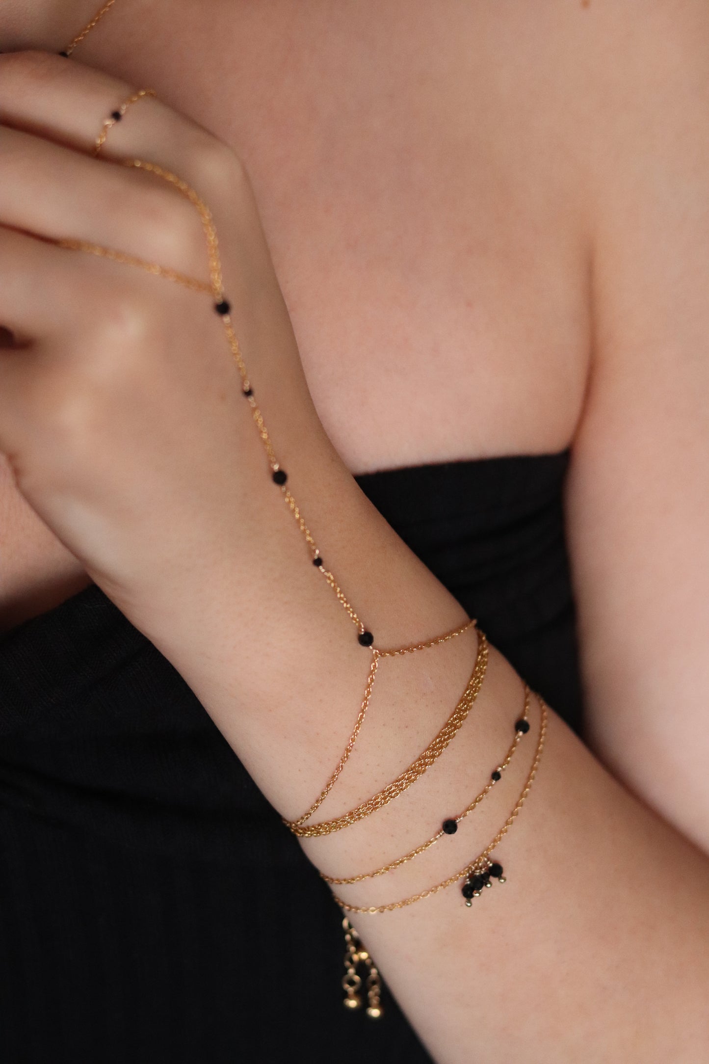 Composition élégante de bijoux en gold-filled, comprenant le bracelet de main Luna, le bracelet Line et le bracelet Lilliane en spinelle noire, accompagnés d'une chaîne collier bracelet Louane, parfaits pour un style chic et intemporel.