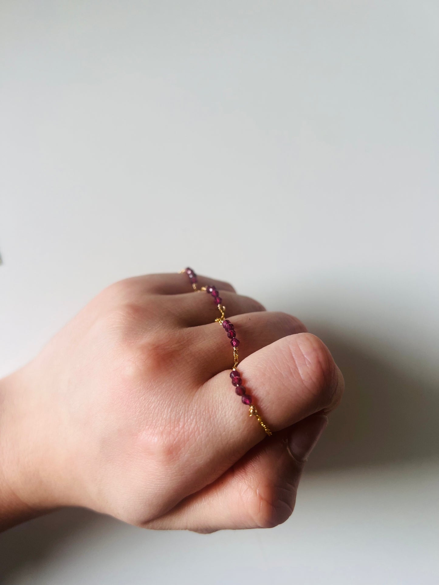 Bague Luna en grenat rouge sur une main, avec une délicate chaîne en gold-filled 14K. Bijou artisanal aux nuances profondes, idéal pour une touche sophistiquée.