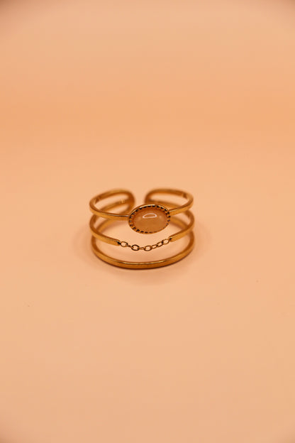 Bague dorée en acier inoxydable à trois anneaux avec médaillon central et fine chaîne décorative
